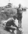 Muž a žena nabírající vodu z řeky, v pozadí kotvící parník, Kikujové