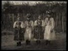 Děti z Cerova ve svátečním kroji, dvě dívky a dva chlapci stojící u dřevěného, laťkového plotu
